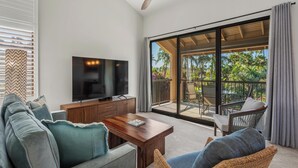 A living room with a flat-screen TV, wooden coffee table, and wicker chairs. - Steps to Keawakapu Beach — Renovated Wailea Condo w/ Pool (Wailea)
