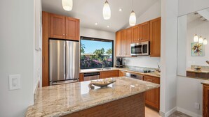 A modern kitchen with wooden cabinets, stainless steel appliances, and a large island. - Steps to Keawakapu Beach — Renovated Wailea Condo w/ Pool (Wailea)