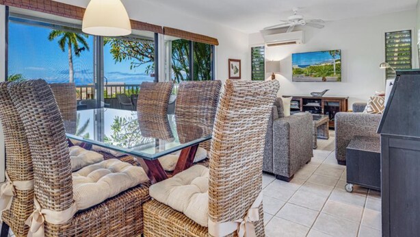 A spacious living area with wicker furniture, a glass-top dining table, and a view of the ocean.