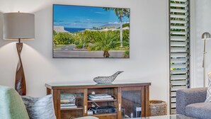 A living room with a flat-screen TV mounted on the wall, a wooden console table with books and decorative items, a glass coffee table, and two sofas.