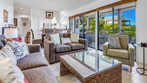 A spacious living area with a large glass sliding door leading to a balcony, furnished with multiple sofas and a coffee table.