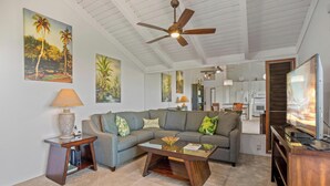 A living room with a grey sectional sofa, a wooden coffee table, a ceiling fan, and a TV on a wooden stand.