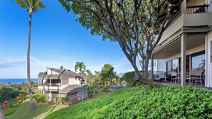 A two-story house with a balcony overlooking a lush garden and a view of the ocean. - Spacious Wailea Condo - Professionally Managed - Ekolu 1607 (Wailea)