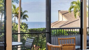 A balcony with a view of the ocean, palm trees, and a building with a tiled roof. - Spacious Wailea Condo - Professionally Managed - Ekolu 1607 (Wailea)