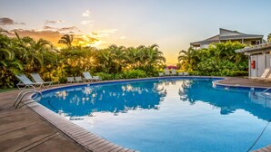 Uma piscina com espreguiçadeiras e palmeiras, cercada por um edifício com design moderno.