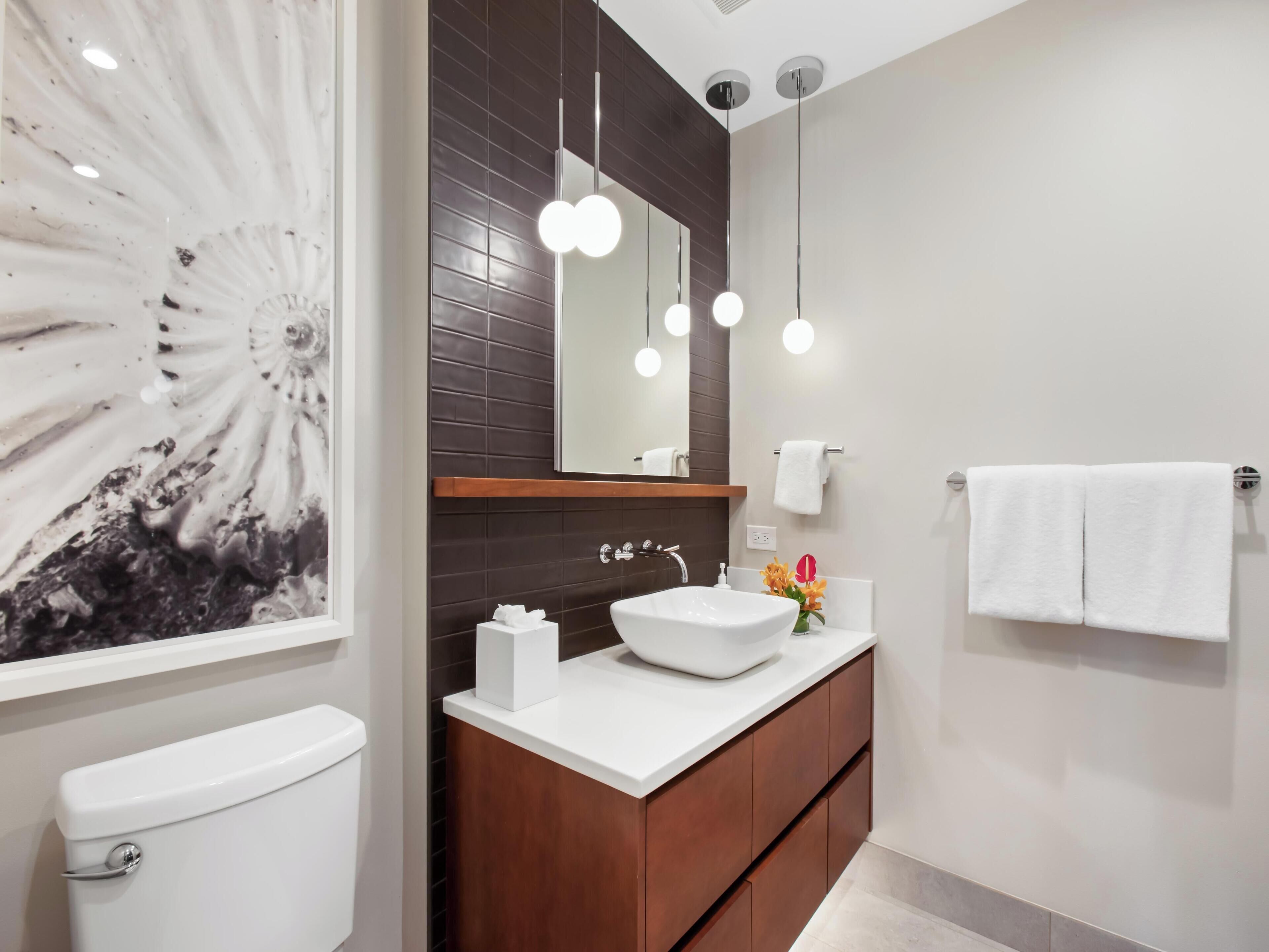 A modern bathroom with a white toilet, a wooden vanity, a large mirror, and a wall-mounted sink.