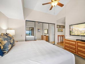 A bedroom with a bed, a ceiling fan, a TV, a dresser, and a sliding door leading to a balcony.