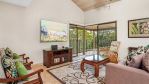 Un salon spacieux doté d’un ventilateur de plafond, d’un grand téléviseur, d’une porte vitrée donnant sur un balcon et d’un coin salon confortable.