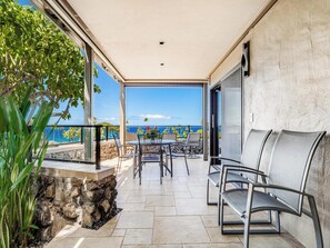 Un balcon agrémenté d’un jardinier en pierre, une table avec des chaises et une vue sur l’océan.