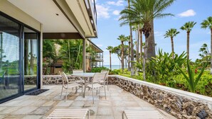 Un patio con una mesa y sillas, un muro de piedra y palmeras.
