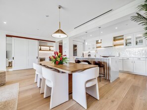 A modern kitchen with white cabinetry, a wooden dining table, and a hanging pendant light. - Oceanfront with Private Plunge Pool (Wailea)
