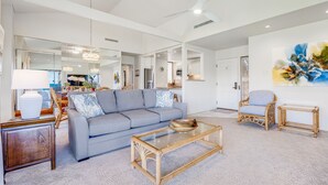 A spacious living room with a grey sofa, a glass coffee table, and wicker chairs.