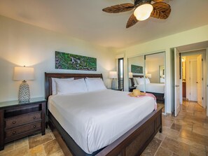 Une chambre spacieuse avec un grand lit, deux tables de chevet avec des lampes, un ventilateur de plafond et un grand miroir.