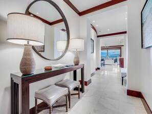Un intérieur moderne avec une console, deux lampes, un miroir, un banc et une vue sur un balcon.