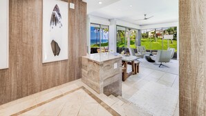 Un interior moderno con un mostrador de recepción de mármol, una obra de arte en grande y vistas a un jardín exuberante y el océano.