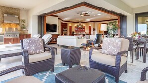 A spacious living area with wicker furniture, a glass coffee table, and a kitchen in the background.