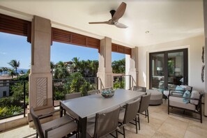 A balcony with a table and chairs, a ceiling fan, and a view of palm trees and buildings.