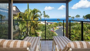 A balcony with two striped lounge chairs, a view of a residential area with palm trees and a road, and a clear blue sky. - Wailea Elua Village 1502 | Ocean View, 2 Min to Ulua Beach, Pools & Pickleball (Wailea)