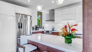 A modern kitchen with white cabinets, stainless steel appliances, a central island with bar stools, and pendant lighting.