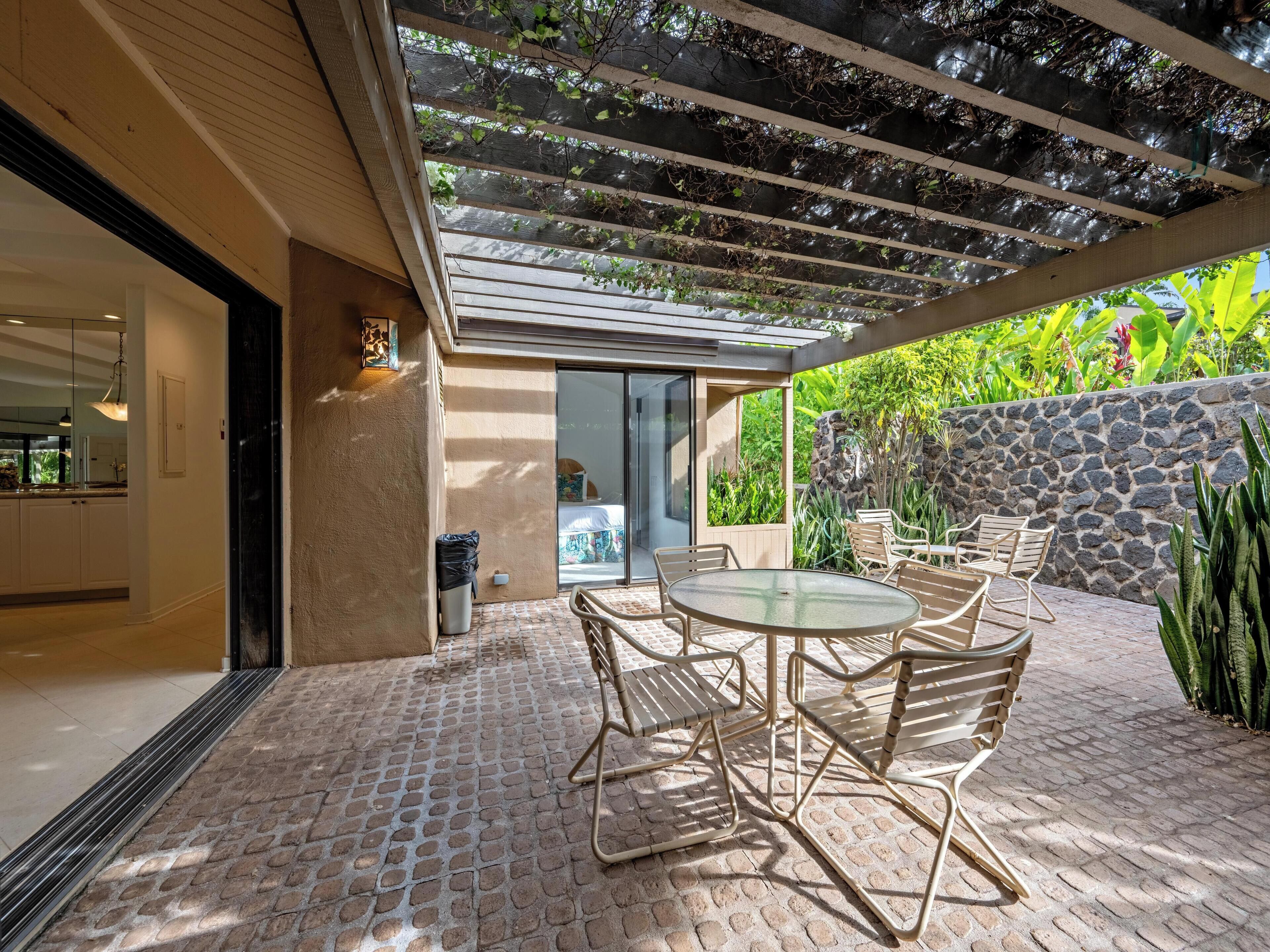 A patio with a round table and chairs, a stone wall, and a pergola with climbing plants.