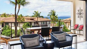 A balcony with two wicker chairs, a small round table, and a red chair. - Wailea Villa Overlooking Lagoon Pool (Wailea)