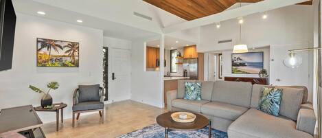 A spacious living area with a wooden ceiling, a large sofa, a coffee table, and a TV.