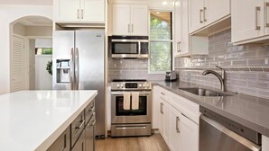 A modern kitchen with stainless steel appliances, white cabinetry, and a grey tiled backsplash.