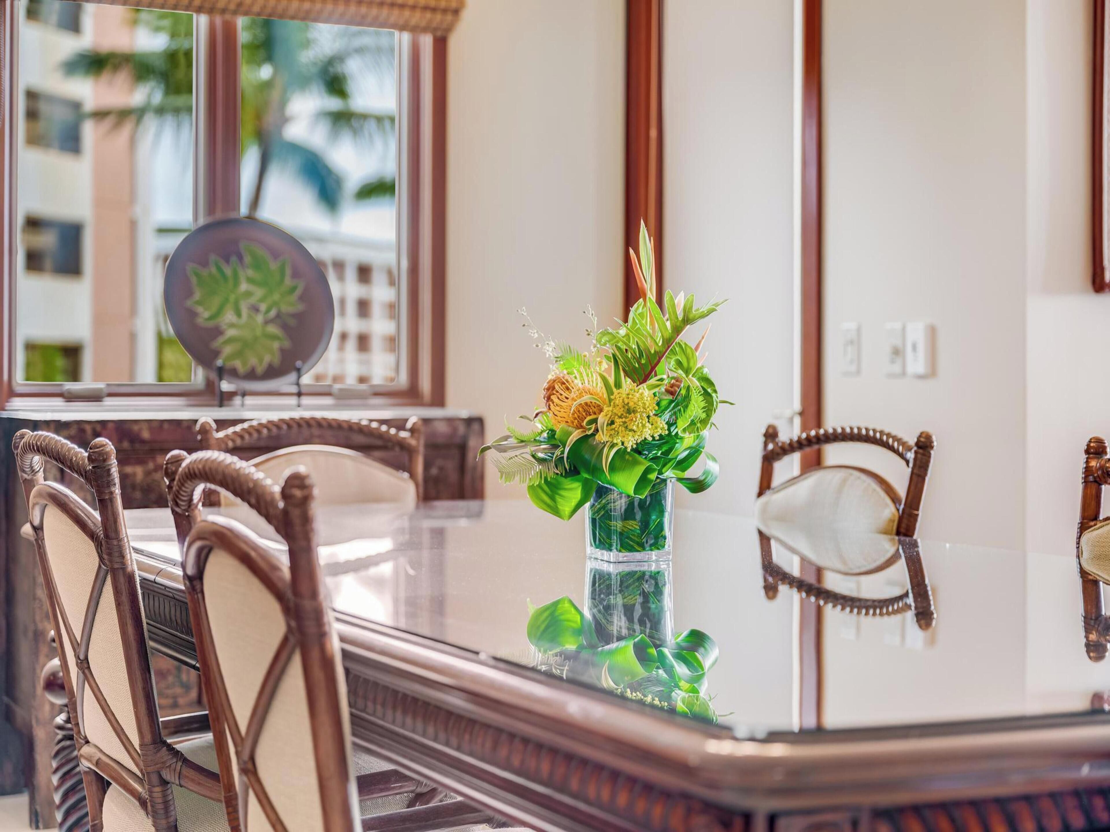 Un coin repas avec une table en verre, des chaises en bois et un vase rempli de fleurs.