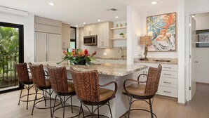 Una cocina moderna con una isla central, cuatro sillas de mimbre y un jarrón decorativo.