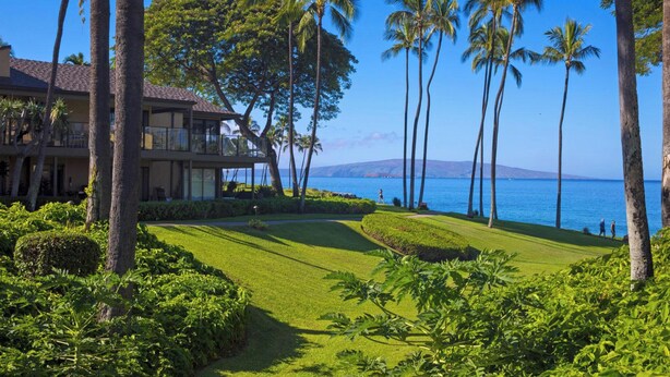 A resort with a well-maintained lawn, palm trees, and a view of the ocean.
