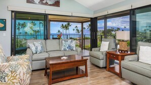 A spacious living room with a large window overlooking a scenic view of palm trees and the ocean. - Recently Renovated - Walk to the Beach (Wailea)