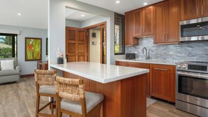 A modern kitchen with wooden cabinets, a stainless steel Bosch oven, and a large island with bar stools. - Recently Renovated - Walk to the Beach (Wailea)