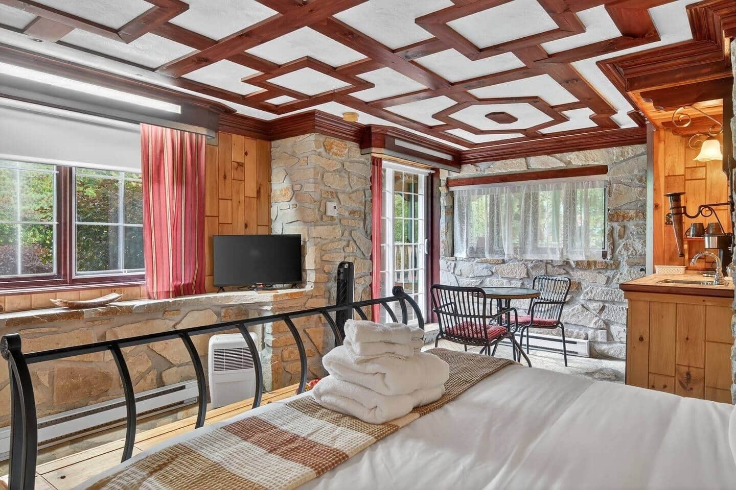 A cozy room with a bed, a TV, a stone wall, and a window with curtains.