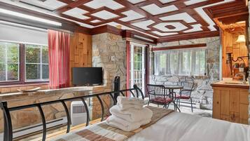 A cozy room with a bed, a TV, a stone wall, and a window with curtains.