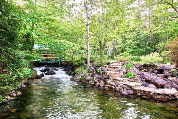 A serene outdoor setting with a small stream, a wooden bridge, and a bench.