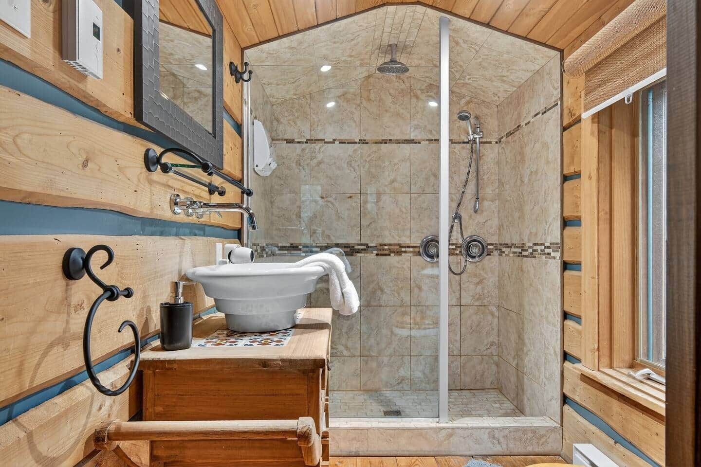 A wooden cabin bathroom with a large sink, a shower, and a mirror.
