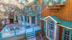 Une maison en bois à plusieurs niveaux, avec des murs en pierre et des touches de couleur turquoise, dotée de nombreux balcons et de grandes fenêtres.