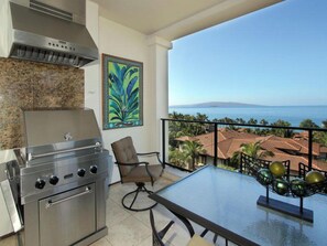 Un balcon avec vue sur la mer, un barbecue, une chaise et une table.