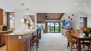 Een ruime keuken met een centraal eiland, houten kastjes en een grote schuifpui die leidt naar een balkon met uitzicht op palmbomen.