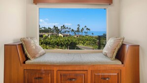 A wooden bench with cushioned seats and storage cabinets, overlooking a beach with palm trees and houses. - Spacious Condo - Great for Families (Wailea)