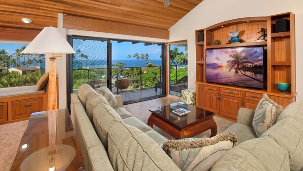 A spacious living room with a large flat-screen TV, wooden ceiling, and a view of the ocean. - Spacious Condo - Great for Families (Wailea)