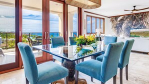 A modern dining area with a glass table and blue upholstered chairs, overlooking a scenic view. - Recently Renovated at Wailea Beach Villas (Wailea)