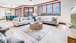 A spacious living room with a large window, a ceiling fan, and a dining area with blue chairs. - Recently Renovated at Wailea Beach Villas (Wailea)