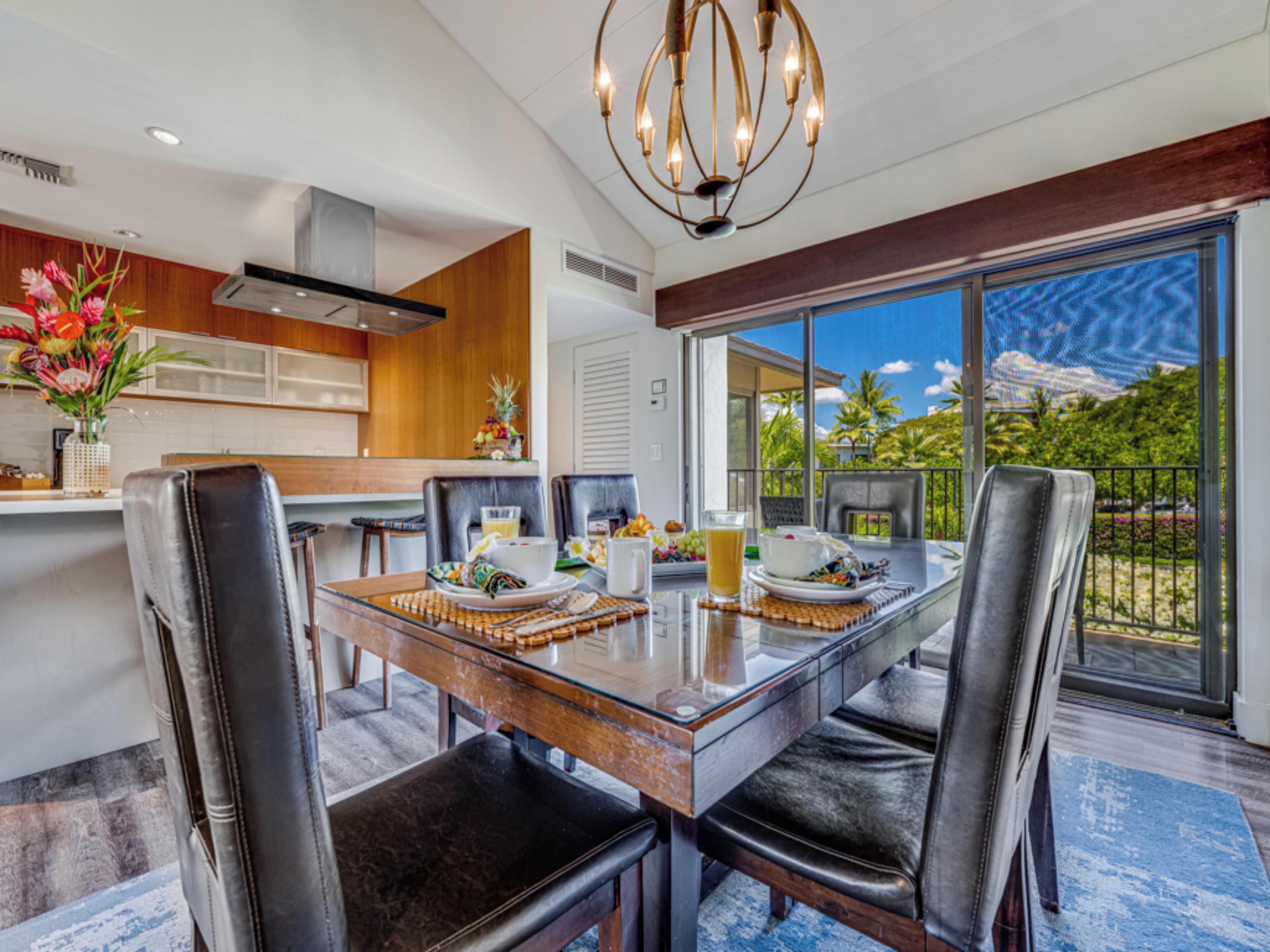 Un espace repas moderne avec une table en verre, des chaises en cuir et une vue sur un paysage tropical grâce à de grandes fenêtres.