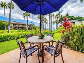 Une table ronde avec quatre chaises, un parasol bleu et un arrangement floral au centre.