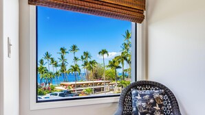 Een kamer met een groot raam dat uitkijkt over een strand met palmbomen en een uitzicht op een gebouw met een zwembad.