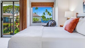 Een hotelkamer met een groot bed, uitzicht op palmbomen en een gebouw door een raam, en een stoel bij het raam.