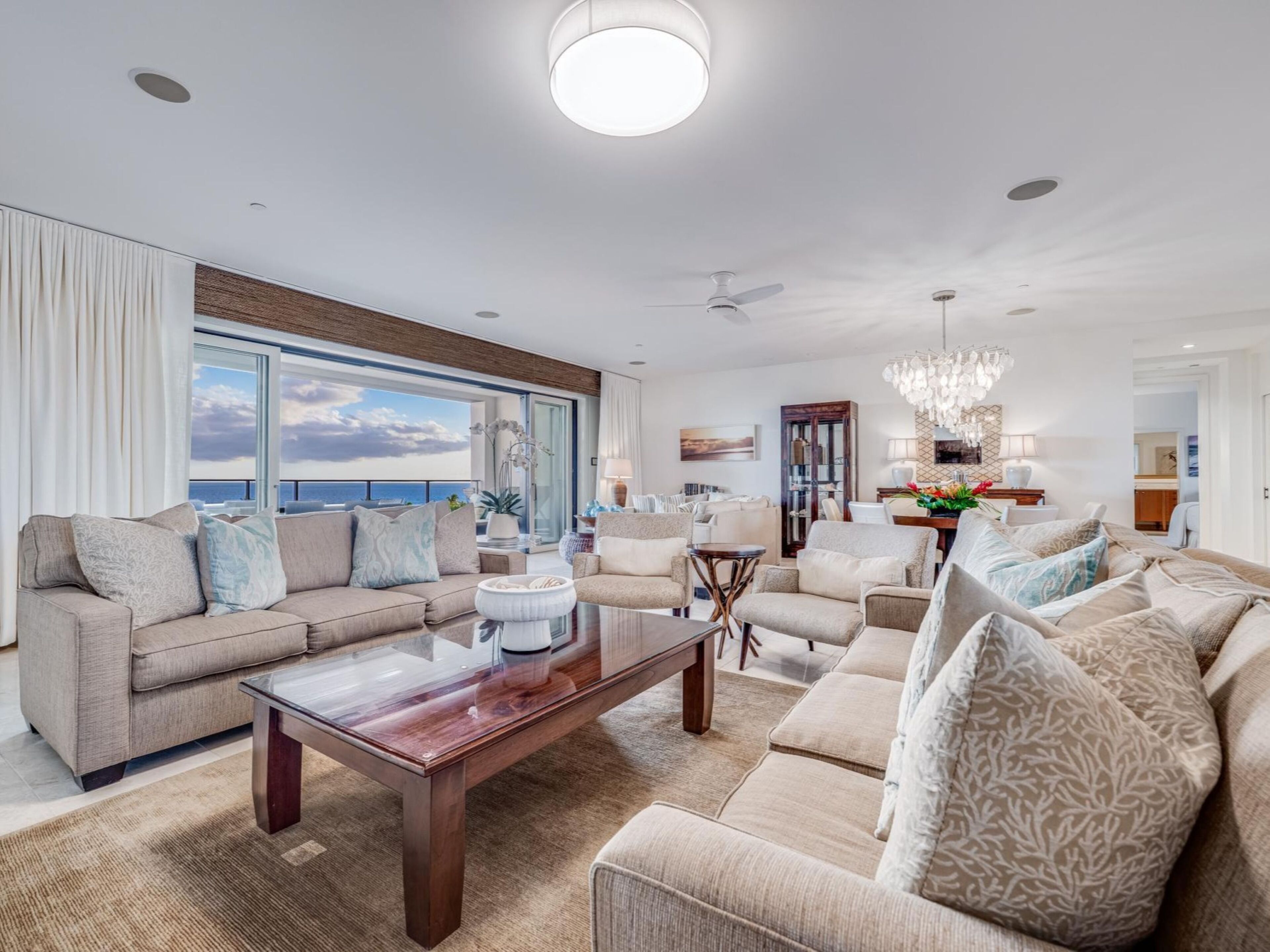 A spacious living room with a large window offering a view of the ocean, a chandelier, and a modern fireplace.