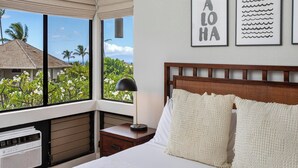 Ein Schlafzimmer mit großem Fenster, einem Bett mit weißer Bettwäsche, einem Holz-Kopfende und zwei gerahmten Bildern an der Wand.