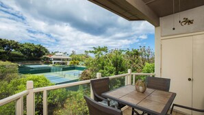 A balcony with a table and chairs, overlooking a tennis court and lush greenery.
